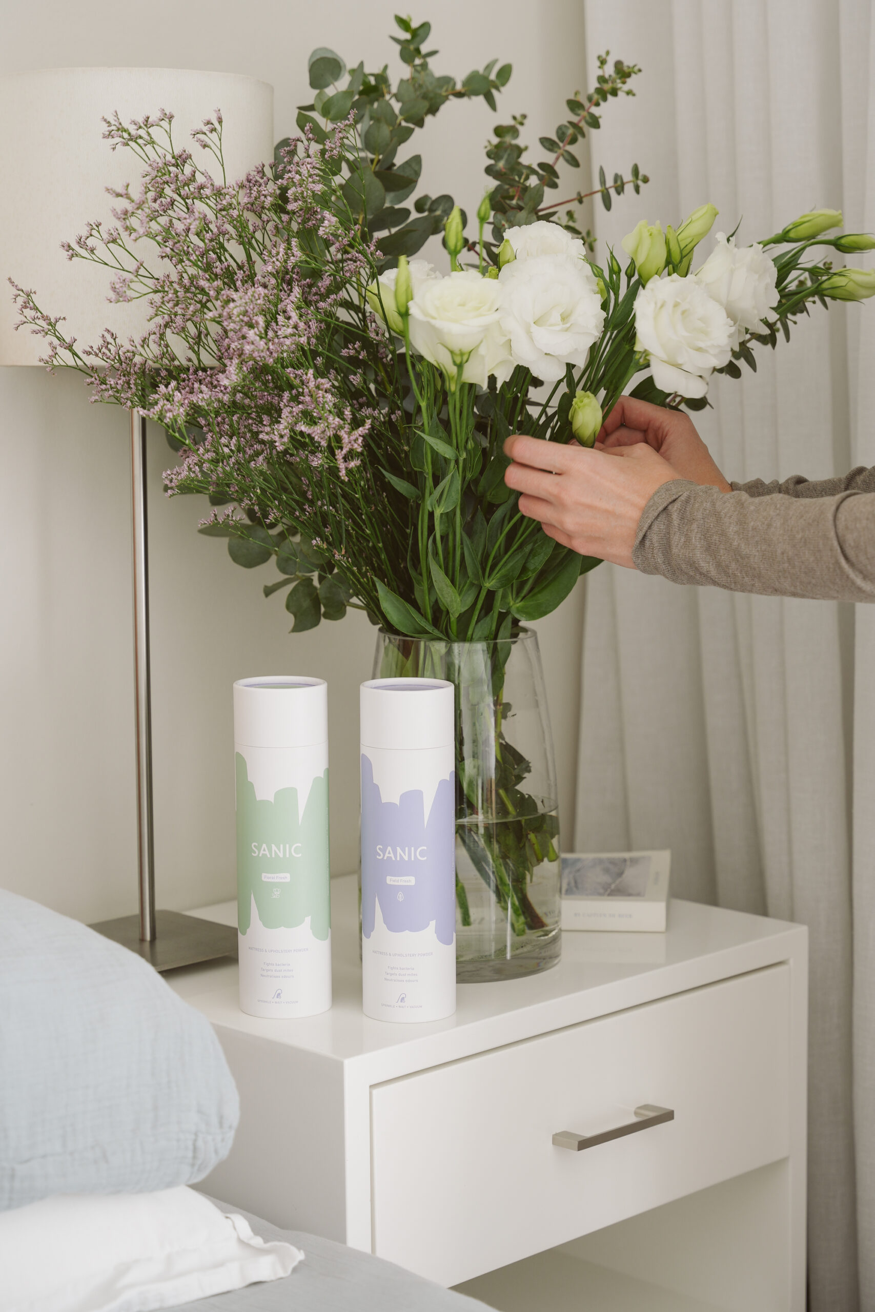 Hands arranging flowers in vase in background. 2 bottles SANIC in foreground.